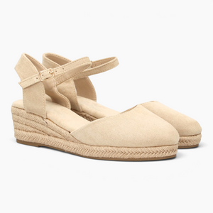 Alpargatas Nuxual de cuña baja en color beige con puntera cerrada, talón abierto y cierre de hebilla en el tobillo.